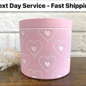 May include: A pink cylindrical container with a white heart pattern. The container has a flat top and bottom and is decorated with white hearts and dotted outlines. The text "Next Day Service - Fast Shipping" is at the top.