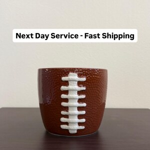 May include: A brown ceramic container designed to resemble a football. The container has a textured surface and white stitching detail. The text "Next Day Service - Fast Shipping" is displayed above the container.