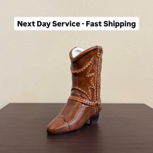 May include: A brown ceramic cowboy boot with white stitching and a star design. The boot has a pointed toe and a small heel. The text "Next Day Service - Fast Shipping" is displayed above the boot.