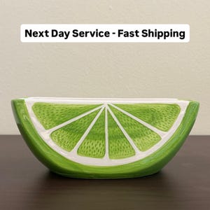 May include: A ceramic bowl shaped like a lime slice, with a bright green exterior and white interior. The bowl has a textured surface and is designed to resemble the segments of a lime. Ideal for serving snacks or as a decorative piece.