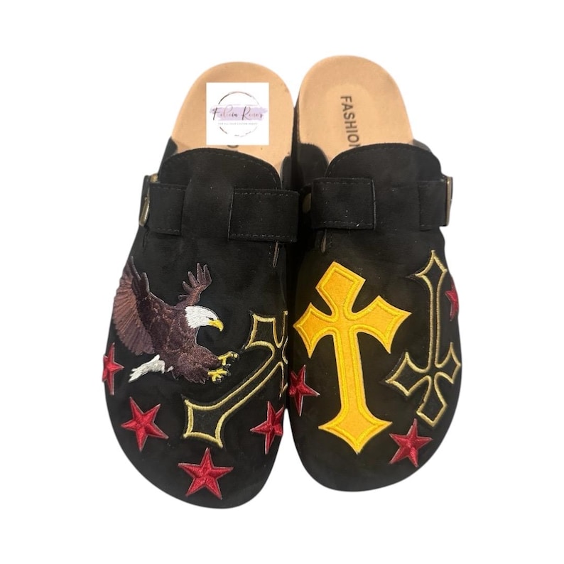 May include: A pair of black suede clogs with embroidered designs. One clog features a yellow cross and the other features a red, white, and blue eagle. Both clogs have red stars and a black strap.