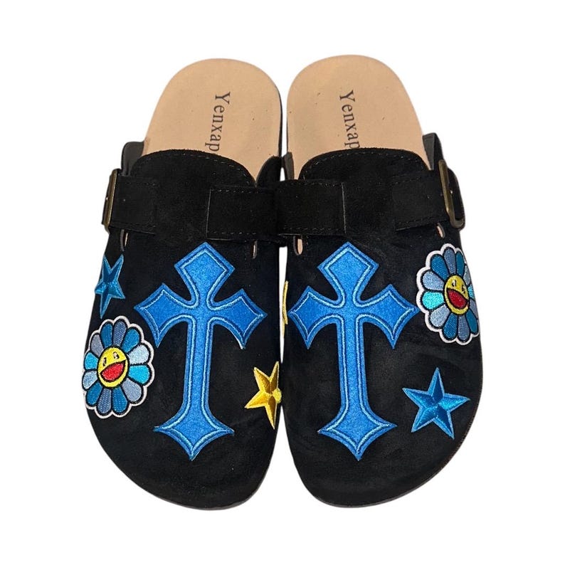 May include: A pair of black suede clogs with a blue cross, yellow star, and blue flower embroidery. The clogs have a buckle strap and the words "Yenxap" are printed on the insole.