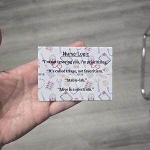 May include: A small, rectangular card with the text "Nurse Logic" and several quotes related to nursing. The card has a white background with medical-themed illustrations and is held in a hand.