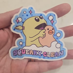 May include: A blue and white sticker with a yellow cartoon character holding a pink duck. The sticker says "SQUEAKY CLEAN" in colorful letters.
