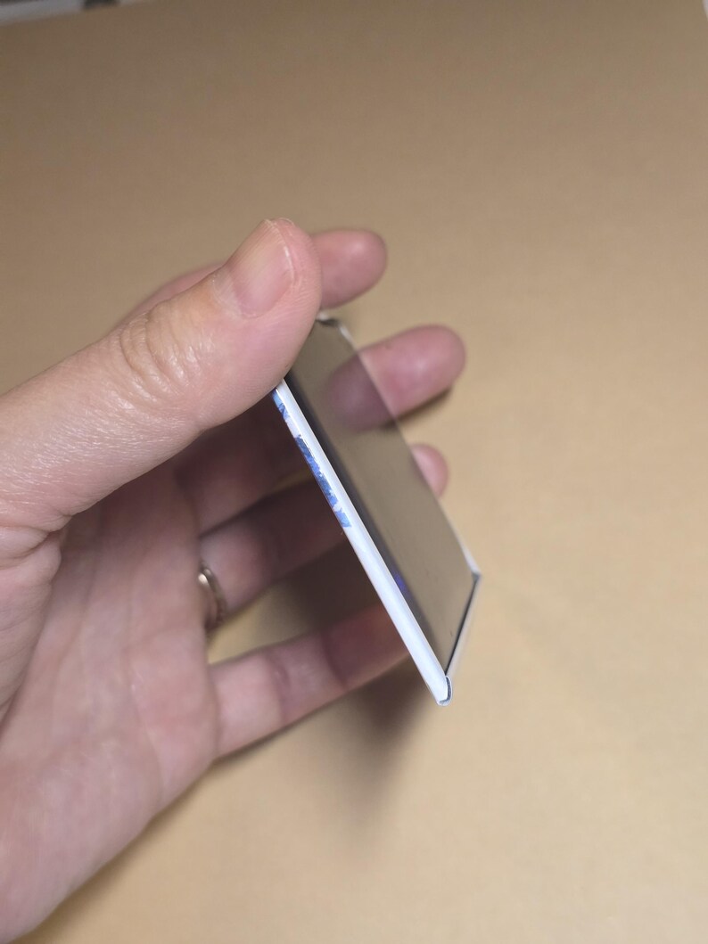 May include: A rectangular magnet with a white border and a glossy black surface. The edge of the magnet shows a hint of blue and white design. The magnet is held in a hand.