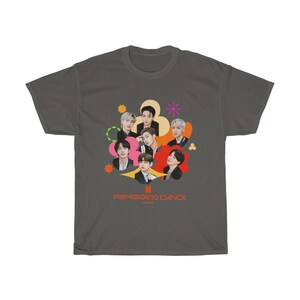 Peut inclure: Un t-shirt gris fonc&eacute; avec un motif color&eacute; de sept hommes dans un design en forme de fleur. Le texte "PERMISSION TO DANCE" est imprim&eacute; sous le graphique.
