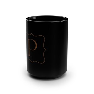 Può includere: Tazza in ceramica nera con un monogramma dorato della lettera "P" in una cornice decorativa.