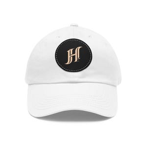 May include: White baseball cap with a curved brim. The cap features a black circular patch with a stitched border. Inside the patch is a stylized, tan letter "H". The cap is made of a soft material and has an adjustable strap.