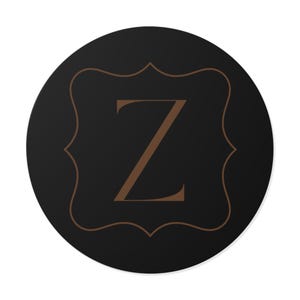 Könnte beinhalten: Ein rundes, schwarzes Emblem mit einem braunen Buchstaben "Z" in einem dekorativen, braun umrandeten Rahmen. Das Design ist auf dem schwarzen Hintergrund zentriert und erzeugt eine schlichte, aber elegante Ästhetik. Geeignet für verschiedene Anwendungen.
