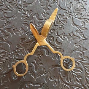 May include: A gold-toned metal cigar cutter with a ring handle. The cutter is open and ready to use.