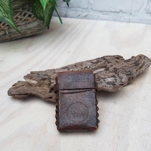Könnte beinhalten: Ein kleines, braunes Lederetui mit Klappverschluss. Das Etui hat ein dekoratives, strukturiertes Design und scheint vintage zu sein.