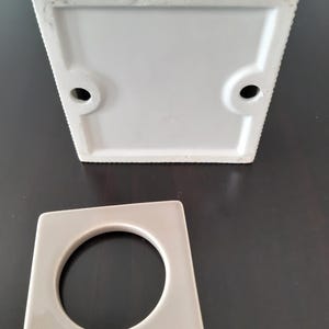 May include: A white ceramic square planter with a round hole in the bottom. The planter is designed to hold a small plant or succulent.