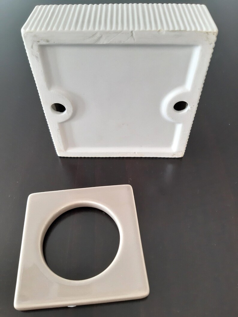 May include: A white ceramic square planter with a round hole in the bottom. The planter is designed to hold a small plant or succulent.
