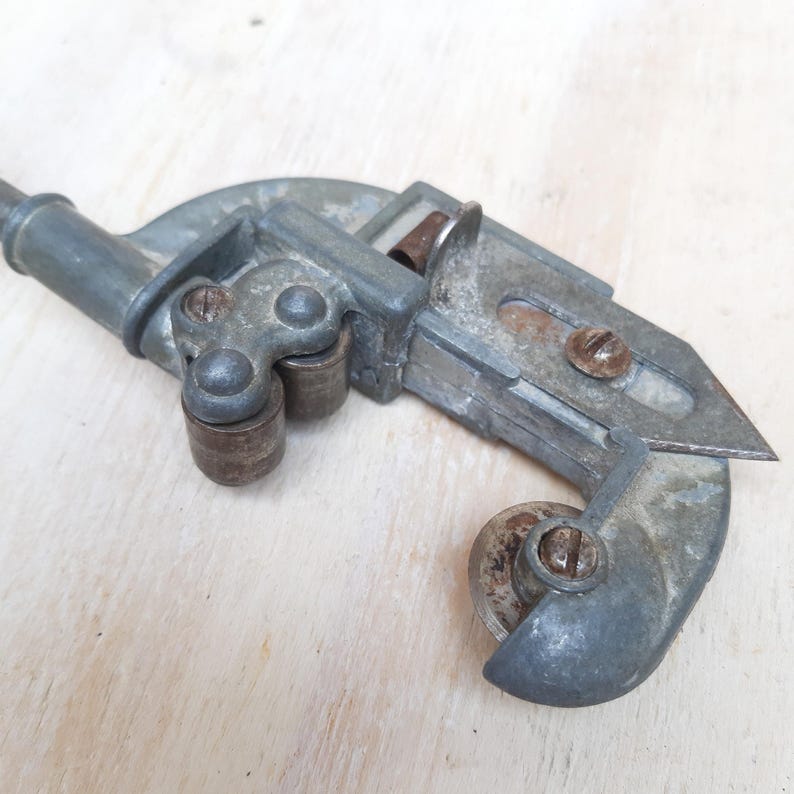 May include: A vintage metal pipe cutter with a silver finish and a black handle. The cutter has two wheels and a blade for cutting pipes.
