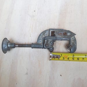 May include: A silver pipe cutter with a black handle and a yellow measuring tape. The tape reads "1 16 FEET 5m 4 5 6 7 8 9 10 11 12 13 14 15 16 17 18 19 20 21 22 23 24 25 26 27 28 29 30 31 32 33 34 35 36 37 38 39 40 41 42 43 44 45 46 47 48 49 50 51 52 53 54 55 56 57 58 59 60 61 62 63 64 65 66 67 68 69 70 71 72 73 74 75 76 77 78 79 80 81 82 83 84 85 86 87 88 89 90 91 92 93 94 95 96 97 98 99 100".