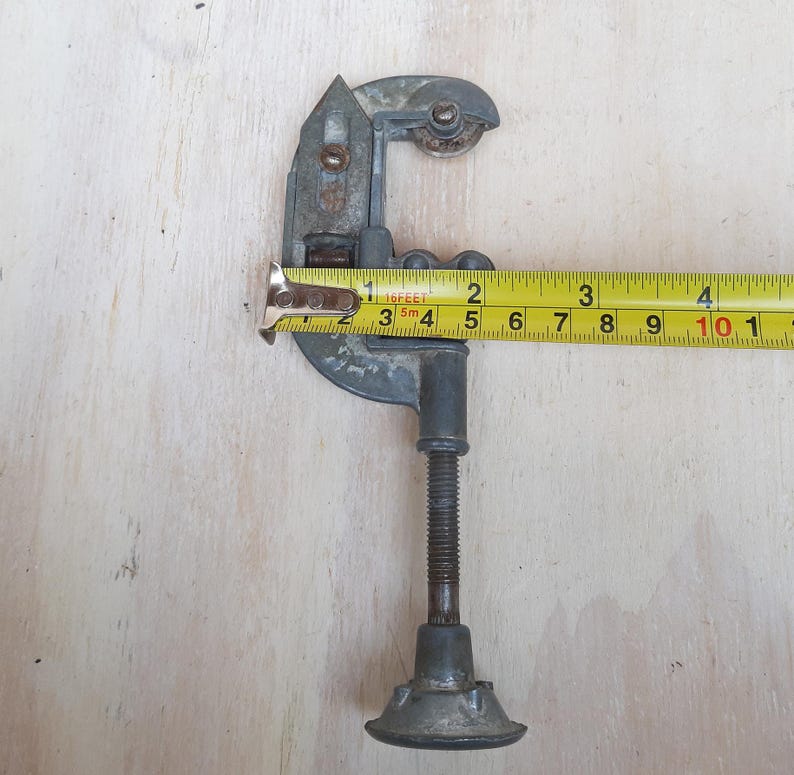 May include: A silver pipe cutter with a black handle and a yellow measuring tape. The tape reads "16 feet" and is marked in inches and centimeters.
