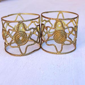 Pu&ograve; includere: Due portatovaglioli in metallo color oro. Ogni anello presenta un design traforato con motivi a spirale e a forma di stella. Gli anelli sono di forma cilindrica e sembrano fatti a mano.