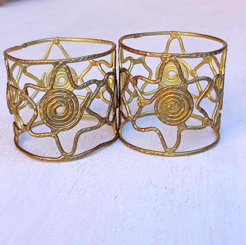 Pu&ograve; includere: Due portatovaglioli in metallo color oro. Ogni anello presenta un design traforato con motivi a spirale e a forma di stella. Gli anelli sono di forma cilindrica e sembrano fatti a mano.