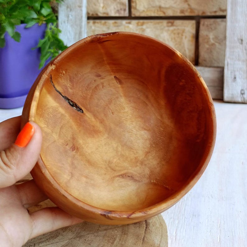 May include: A round wooden bowl with a smooth, polished finish, showcasing natural light brown wood grain patterns and a distinct dark, thin crack running across the interior surface, highlighting the organic texture of the material.