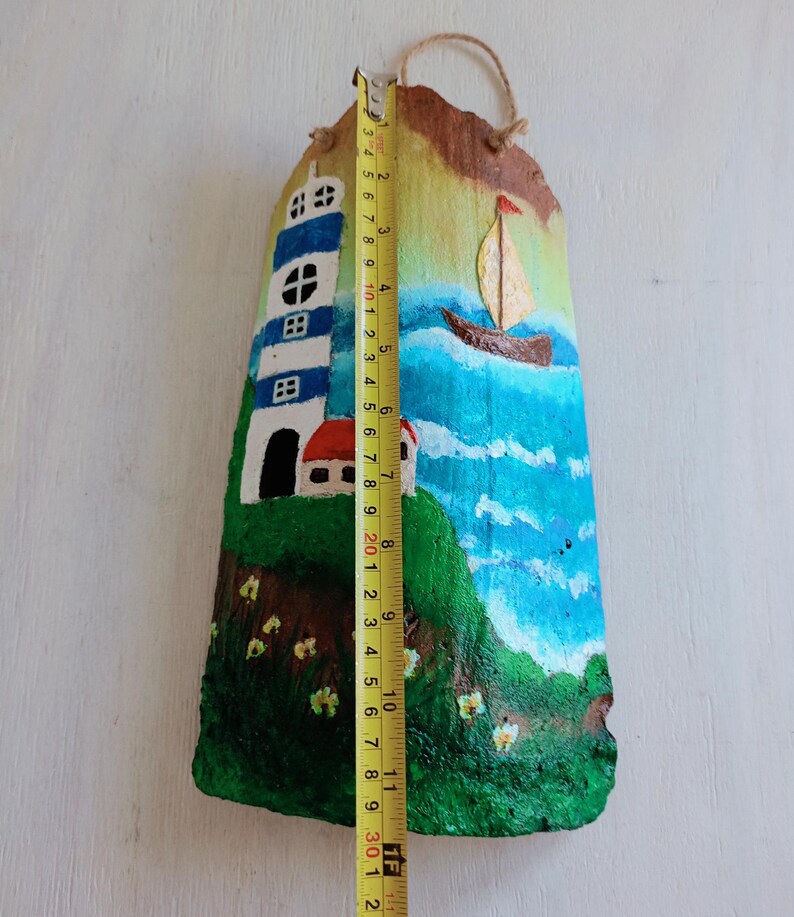 May include: Hand-painted coconut shell art depicting a lighthouse, a small house, a sailboat, and a blue ocean with white clouds. The coconut shell is approximately 30 cm tall.