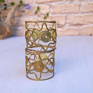 Pu&ograve; includere: Due braccialetti a polsino in metallo color oro. I braccialetti sono impilati l'uno sull'altro. Ogni braccialetto presenta un design traforato con motivi a spirale e lineari. I braccialetti sono esposti su uno sfondo neutro.