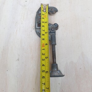 May include: A silver pipe cutter with a yellow measuring tape next to it. The tape measures 7 inches.