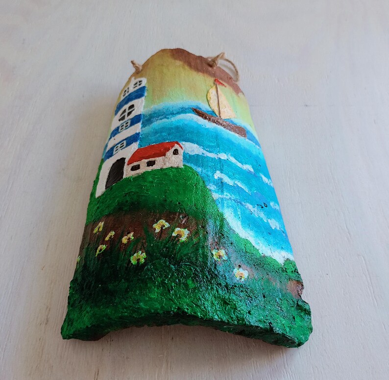 May include: Hand-painted wooden seascape with a lighthouse, a small house, a sailboat, and green grass with yellow flowers. The background is a blue ocean with white waves.
