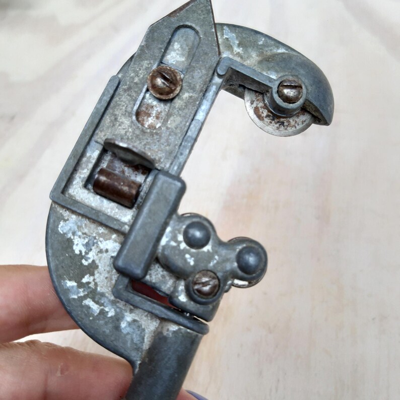 May include: A vintage metal pipe cutter with a silver finish and rust spots. The cutter has a handle and a rotating blade.