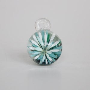 May include: A glass ornament with a white and blue flower design inside. The ornament has a clear glass loop at the top for hanging.