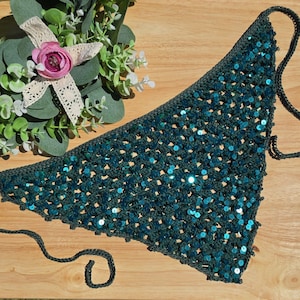 May include: A triangular crochet bandana in a deep teal color, featuring a dense pattern of shimmering, reflective sequins throughout the fabric. The accessory includes thin, matching crochet ties at the corners for securing the garment.