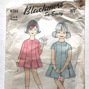 Op de afbeelding: Vintage naaipatroon voor een meisjesjurk. Het patroon is voor maten 7 tot 8 jaar. Het patroon heet "Blackmore So-Easy" en het patroonnummer is 9701. Het patroon toont twee meisjes die de jurk dragen, een in roze en een in blauw.