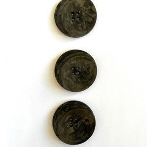 Peut inclure: Trois boutons marbrés noirs et gris avec quatre trous chacun.