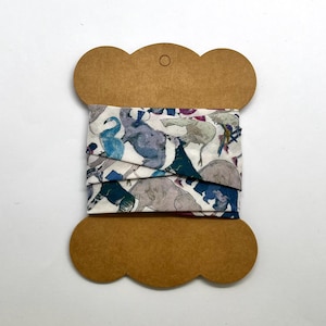 May include: A roll of white fabric with a colorful print of birds and elephants on a brown cardboard spool.
