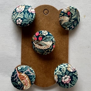 May include: Five fabric-covered buttons with a botanical design featuring birds, flowers, and berries in teal, pink, and cream. The buttons are arranged on a brown card, ideal for craft projects. Each button has a diameter of approximately 2.5 cm.