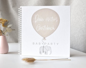Könnte beinhalten: Ein weißes Gästebuch mit einem rosafarbenen Ballon und einer Elefantenillustration. Der Ballon trägt den Text "Dein erstes Gästebuch" und der Text "BABY PARTY" befindet sich unter dem Elefanten.