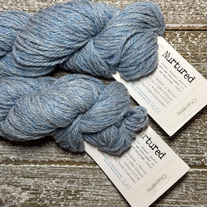 May include: A skein of light blue yarn called "Nurtured" by Chambray. The yarn is a blend of Targhee and Merino wool. The label states that the yarn is 118 meters (130 yards) and is recommended to be knit with needles sized 4-5 mm (US 6-8). The yarn should be washed in cold water.