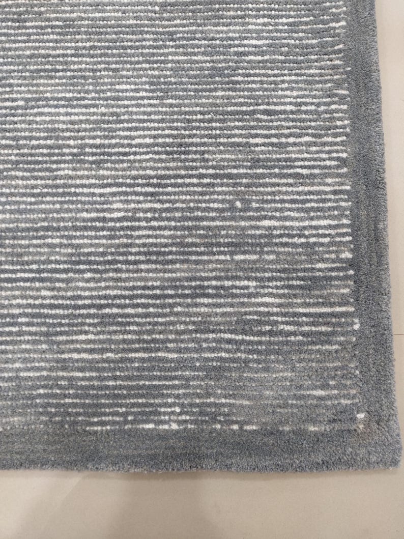 May include: A close-up of a gray and white striped rug with a gray border. The rug has a soft, textured feel.