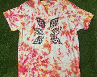 May include: A tie-dye t-shirt with a red, yellow, and white swirl pattern. The shirt features a black graphic of six stylized eyes with a black and white design. The text "Cosmos Designs" is printed in black at the bottom of the shirt.