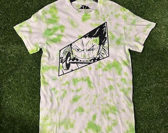 May include: A green and white tie-dye t-shirt with a black and white illustration of a character from the anime One Piece. The character is holding a sword and has a serious expression on their face. The text "Cosmos Designs" is printed on the bottom of the shirt.