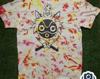 May include: White tie-dye t-shirt with a graphic of a mask, knives, and a forest spirit. The design is in black, with yellow and red tie-dye patterns throughout the shirt. The shirt is short-sleeved.