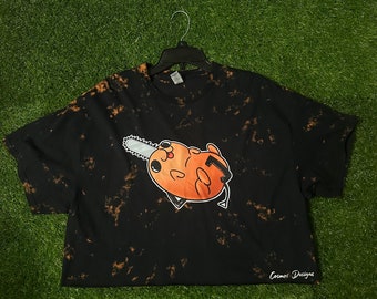 May include: Black tie-dye t-shirt with a cartoon illustration of a brown creature holding a chainsaw. The text "Cosmos Designs" is printed on the bottom right corner of the shirt.