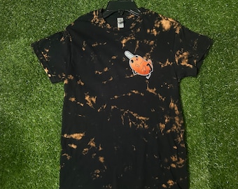 May include: Black t-shirt with a bleach tie-dye pattern. The shirt features a cartoon image of a pig holding a chainsaw.