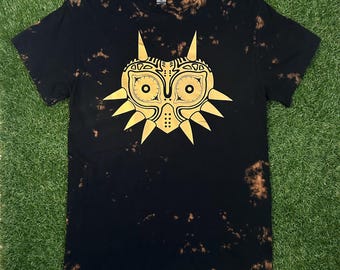 May include: Black t-shirt with a gold Majora's Mask design. The shirt has a bleach-splattered effect.