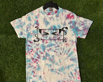 May include: A tie-dye t-shirt with a white base and blue and red swirls. The shirt features a graphic of anime eyes within a black rectangular frame. The text "Cosmos Designs" is printed at the bottom right.