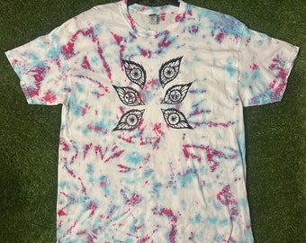 May include: A white t-shirt with a tie-dye pattern in shades of blue and pink. The shirt features a black graphic of six stylized eyes with wings.