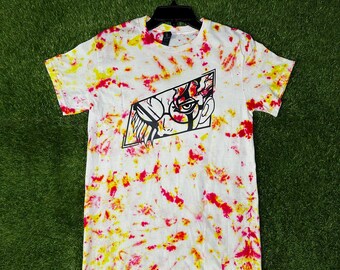 May include: White tie-dye t-shirt with a black graphic of a face inside a geometric shape. The shirt has red and yellow splashes throughout and the words "Cosmic Designs" are printed at the bottom.