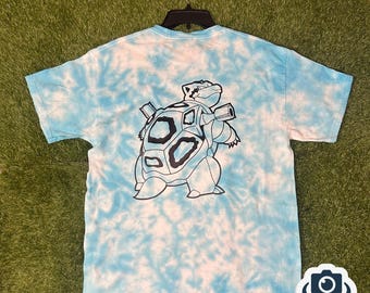 May include: A blue and white tie-dye t-shirt with a black and white graphic of a turtle with guns on its back.