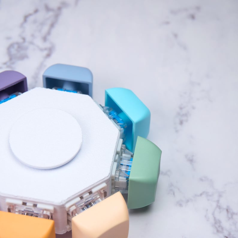 May include: A multi-colored, octagonal device with a white central disc. The device has various pastel-colored components, including blue, green, orange, and purple. The background is a marble-patterned surface.