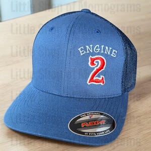 May include: A blue and black baseball cap with a white embroidered patch that says "ENGINE 2" in white with a red number 2. The cap has a Flexfit label on the underside of the brim.