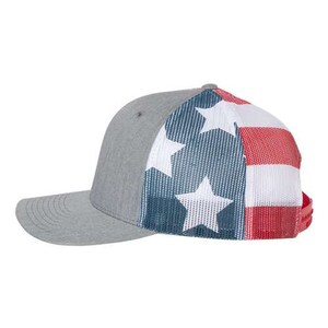 May include: A gray and white trucker hat with a red, white, and blue American flag design on the back. The hat has a mesh back and a curved brim.